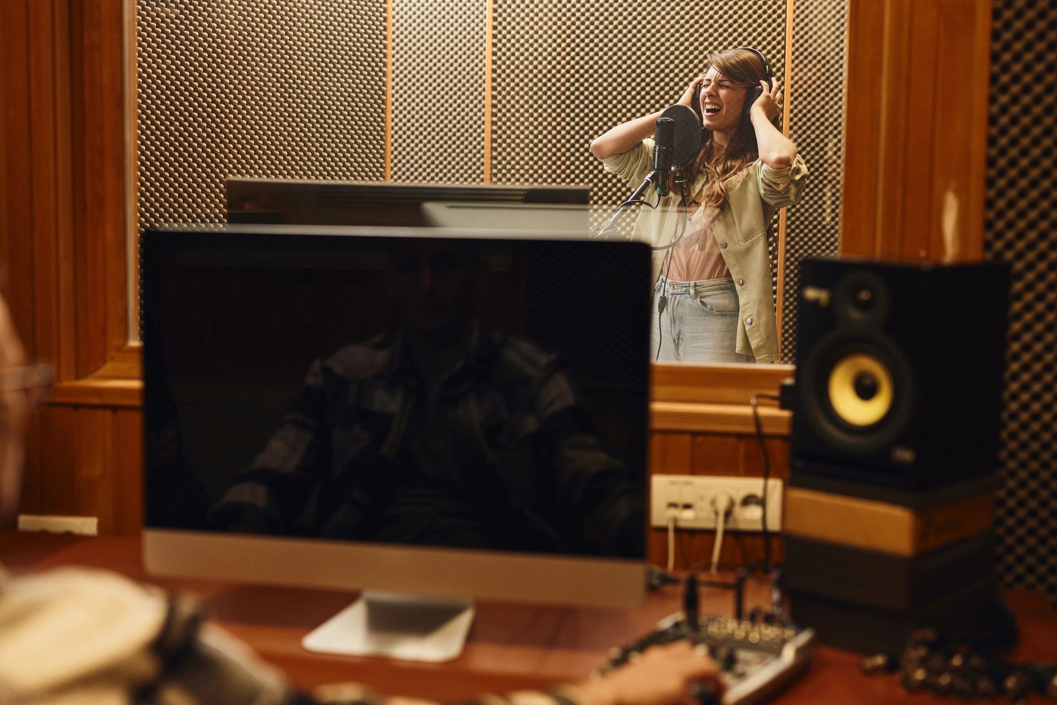 Artist recording vocals in a professional studio behind glass